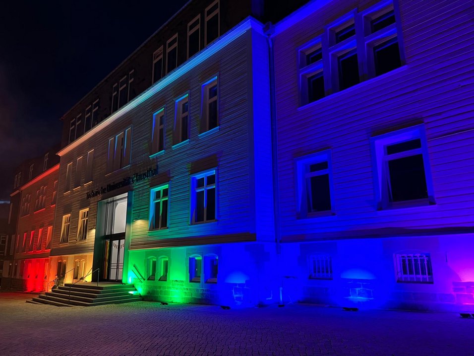 Auf diesem Bild ist das abendliche TU Clausthal Hauptgebäude angestrahlt mit Regenbogenfarben zu sehen.